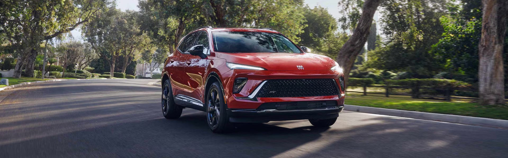 Red Buick SUV driving on a tree-lined road with a modern exterior design.