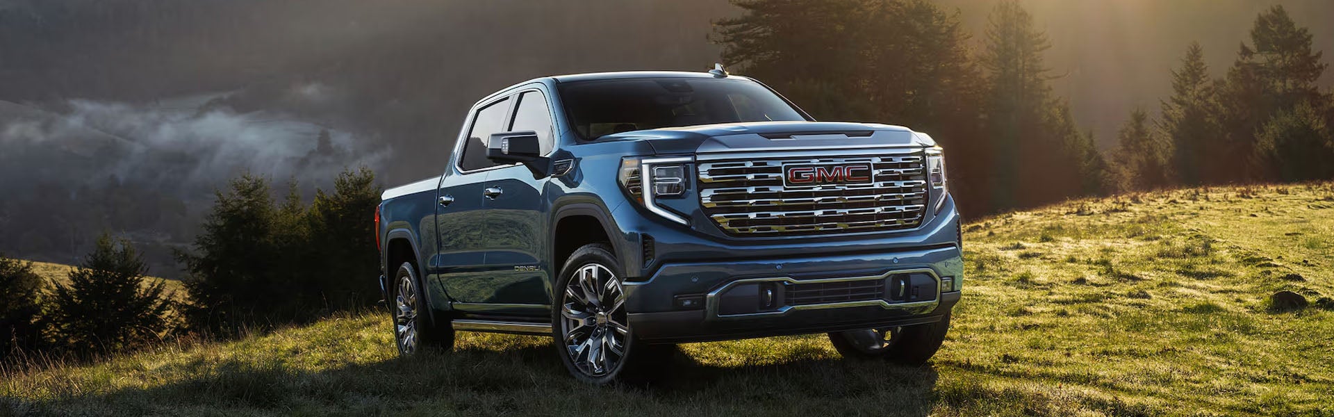 Blue GMC Sierra pickup truck in a mountain landscape.